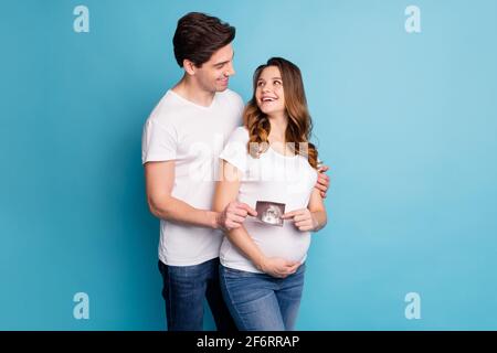 Foto von jungen glücklich aufgeregt positive lächelnde Familie halten Ultraschall Bild von Baby isoliert auf blauem Hintergrund Stockfoto