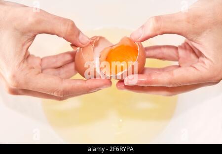 Kuchenherstellung: Hände öffnen ein Ei mit einem roten Eigelb im Inneren. Rom, Italien, 1. Mai 2020 Stockfoto