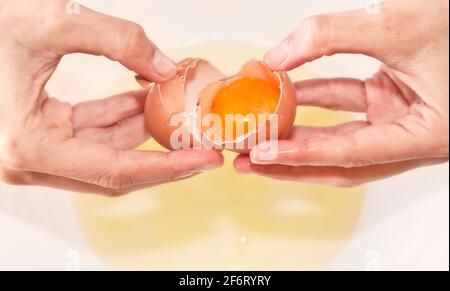 Kuchenherstellung: Hände öffnen ein Ei mit einem roten Eigelb im Inneren. Rom, Italien, 1. Mai 2020 Stockfoto