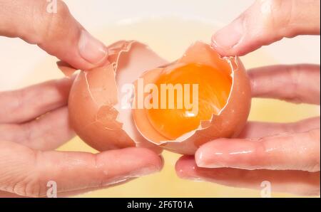 Kuchenherstellung: Hände öffnen ein Ei mit einem roten Eigelb im Inneren. Rom, Italien, 1. Mai 2020 Stockfoto