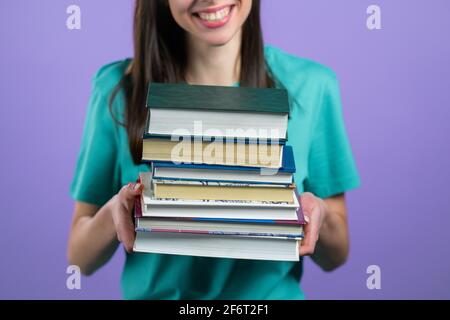 Studentin hält Stapel von Universitätsbüchern aus der Bibliothek auf violettem Hintergrund im Studio. Nicht erkennbare Frau. Stockfoto