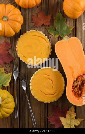 Traditionelles Thanksgiving Dessert Offene Kürbiskuchen mit zwei Gabeln, leuchtend orangefarbenen Kürbissen und marmorblättern auf Vintage-Holzhintergrund oben serviert Stockfoto