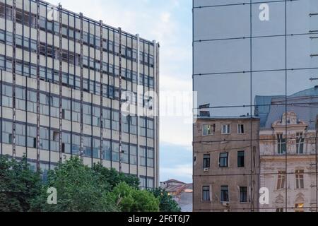 Alte klassische Gebäude spiegeln sich im modernen Glasgebäude wider, im Hintergrund das Gebäude der sozialistischen Moderne, Bukarest, Rumänien Stockfoto