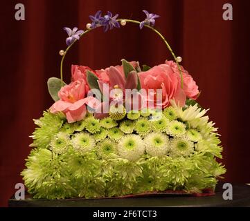 Blumenstrauß im Osterthema mit grünen Chrysanthemen, rosa Blumen und Griff, der mit violetten Blumen geschmückt ist Stockfoto
