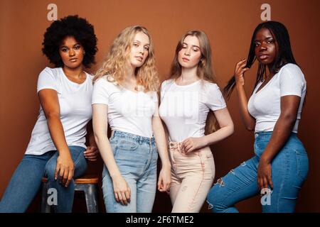 Junge hübsche kaukasische, afro, skandinavische Frau posiert fröhlich zusammen auf braunem Hintergrund, Lifestyle diverse Nationalität Menschen Konzept Stockfoto