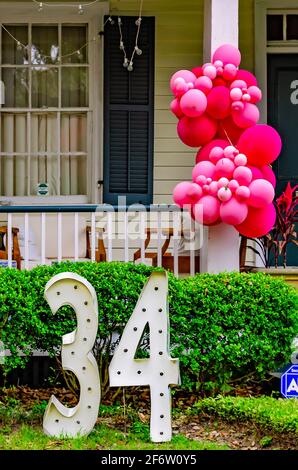 Luftballons, die an einem Geländer auf der Veranda hängen, und eine große Zahl von „34“ auf dem Rasen markieren den Geburtstag eines Einheimischen am 30. März 2021 in Mobile, Alabama. Stockfoto