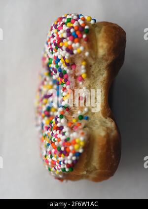 Ein vertikales Bild eines Bonbons streuen überzogenen Donut mit Ein Biss aus dem Gebäck Stockfoto