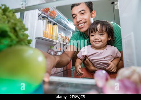 Das kleine Mädchen und ihr Vater schauten in den Kühlschrank Stockfoto