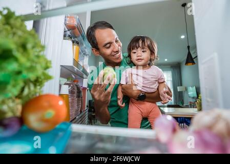 Das kleine Mädchen und ihr Vater schauten in den Kühlschrank Stockfoto