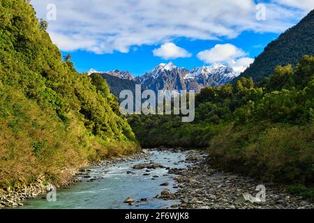Türkisfarbener Wasserbach und Flussfelsen, die zwischen den Bergen fließen, in der Mitte des Bildes gibt es eine schneebedeckte Bergspitze, natürliche Aussicht in der Stockfoto