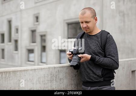 Porträt eines männlichen Fotografen oder Videofilmer, der Videos oder Fotos ansieht Auf seiner Kamera über dem Betonbauhintergrund Stockfoto