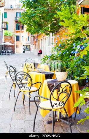 Süßes kleines Café im Freien in Venedig, Italien, mit gelben Tischen und schleichenden Reben an der Wand Stockfoto