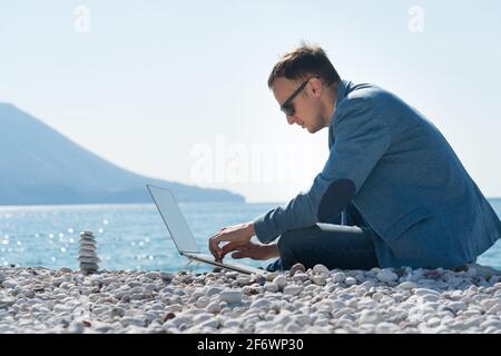 Freiberuflicher Geschäftsmann, der am Strand in der Nähe an einem Laptop arbeitet Die Zen-Pyramide Stockfoto