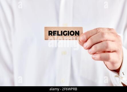 Männliche Hand hält einen Holzblock mit dem Wort Religion. Stockfoto