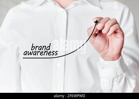 Businessman mit Stift zeichnet eine steigende Liniengrafik mit dem Wort Markenbekanntheit auf einem virtuellen Bildschirm. Konzept zur Steigerung des Markenbewusstseins. Stockfoto