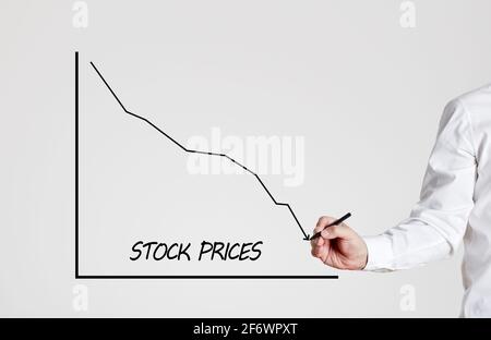 Businessman zeichnet ein abnehmendes Liniendiagramm mit dem Wort Aktienkurse. Wirtschaftskrise und sinkende Aktienkurse. Stockfoto