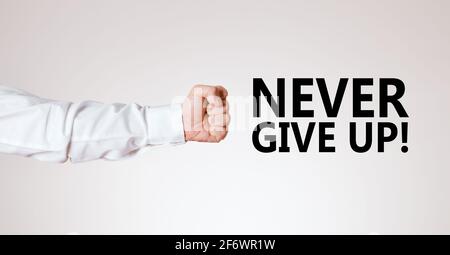 Männlicher Arm mit der Hand als geballte Faust zeigt auf die motivierende Botschaft nie aufgeben. Entschlossenheit und Persistenz Konzept. Stockfoto