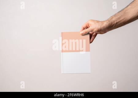 Männliche Hand hält einen geschlossenen Buch-Katalog mit leerem Cover, editierbare Modell-up-Serie Vorlage bereit für Ihr Design, Cover-Auswahl-Pfad enthalten. Stockfoto