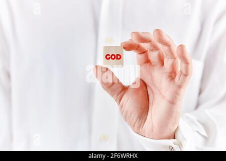 Männliche Hand hält einen Holzwürfel mit dem Wort gott. Religion und Gottesdienst Konzept. Stockfoto