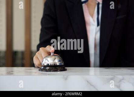 Nahaufnahme einer Geschäftsfrau, die an der Rezeption silberne Klingel klingelt. Stockfoto