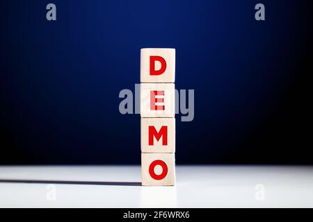 Das Wort Demo auf gestufte Holzwürfel vor blauem Hintergrund geschrieben. Akronym für Demonstration. Stockfoto