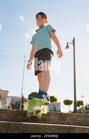 Glücklicher kleiner Junge, der im Park auf Skateboard spielt, kaukasisches Kind, das Penny Board reitet, Skateboard übt. Stockfoto