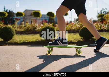 Nahaufnahme Beine in blauen Sneakers Reiten auf grünem Skateboard in Bewegung. Aktive urbane Lebensweise der Jugend, Training, Hobby, Aktivität Stockfoto