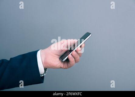 Ein Mann Geschäftsmann in Anzug gekleidet hält Smartphone vor grauem Hintergrund. Geschäftskonzept. Stockfoto