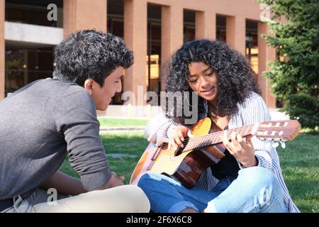 Ein junger lateinmann lehrt einer jungen lateinerin auf dem Universitätscampus, wie man Gitarre spielt. Universitätsleben, tausendjährige Generation. Stockfoto