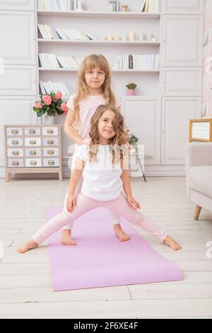 Vertikale Foto von paar kleinen Mädchen spielen auf Yoga-Matte lächeln im Wohnzimmer, gesunde Lebensgewohnheiten und Lifestyle-Konzept. Stockfoto