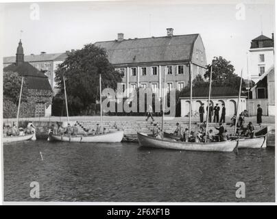 Das Bild zeigt vier Segelboote, die am Kai von Kungsbron festgemacht sind. In jedem Boot Geist eine Crew, die die Boote vor oder nach dem Segeln vorbereitet. Auf dem Dock, vier höhere Kommandeure, während ein fünfter Befehl ist in der Vorderseite der beiden Boote, die ganz rechts im Bild sind. Es ist jedoch nicht möglich, einzelne Merkmale dieser oder der Wissenschaft zu unterscheiden. Oben am Kai gibt es auch drei Lebensmittelrosen: Zwei sitzen im Bild rechts am Kai und einer geht auf den Kai. Im Hintergrund sind die Residenz Garage und von Otherska Hof zu sehen .. Das Bild zeigt vier Segelboot Stockfoto