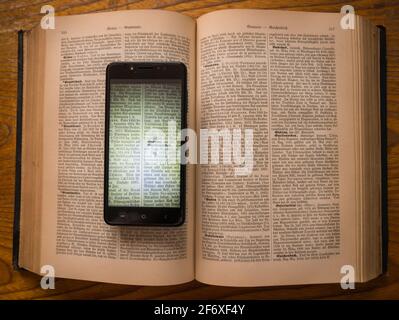 Smartphone mit einer digitalen Kopie eines mehr als 100 Jahre alten Buches liegt auf dem Original. Stockfoto