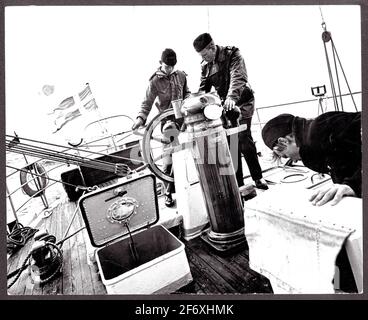 Das Bild zeigt drei Seeleute auf dem Heckschiff des Schulschiffes Falcon während der Segeltörns. In der Mitte des Bildes, Schiffsmanager Lars Haller scheint einen Kadett zu lehren, der das Lenkrad hält.das Schiff greift frei zur Steuerbord-Seite.das Bild zeigt drei Matrosen auf dem Heckschiff des Schulschiffes Falcon während des Segelns.in der Mitte des Bildes, Schiffsmanager Lars Haller scheint einen Kadett zu lehren, der das Lenkrad hält.das Schiff greift frei zur Steuerbord-Seite Stockfoto