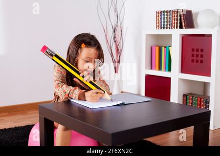 Kleines Mädchen in ihrem Haus mit einem riesigen Bleistift schreiben Stockfoto