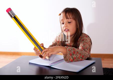 Kleines Mädchen in ihrem Haus mit einem riesigen Bleistift schreiben Stockfoto