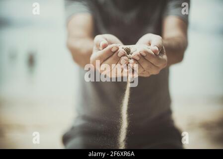 Mann, der am Strand steht und Sand durch seine Hände läuft, Thailand Stockfoto