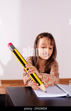 Kleines Mädchen in ihrem Haus mit einem riesigen Bleistift schreiben Stockfoto