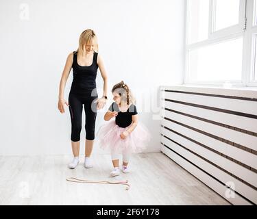 Frau Mutter gibt sich dem Tanzen mit ihrer kleinen Tochter, ist in der Gymnastik in einem weißen Interieur, Lifestyle-Foto beschäftigt Stockfoto