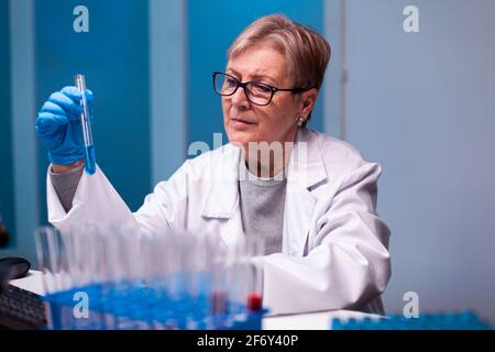 Leitender Wissenschaftler, der die Probe mit Chemikalien in einem Reagenzglas mit Handschuhen und Schutzbrille aufnimmt. Doktor in White Coat Forschung ein neues Experiment im Labor, das biotechnologische Arbeiten mit modernen Geräten analysiert. Stockfoto