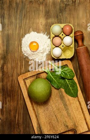 Grünes Teigbrötchen für die Herstellung von Nudeln, zubereitet auf dem Tisch mit Zutaten, traditionelle italienische Küche Stockfoto