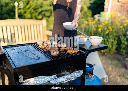 Nahaufnahme eines Mannes, der Hühnerflügel mit bbq würzt Auf einem gasgrill Stockfoto