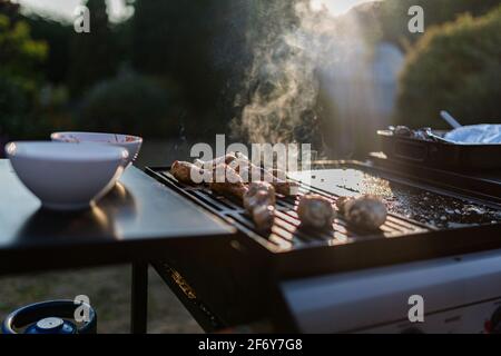 Nahaufnahme eines bbq-Grills mit Fleisch auf ihnen kochen, Sonneneinstrahlung im Hintergrund fängt den Rauch auf Stockfoto