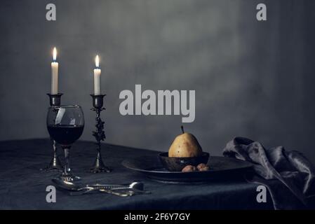 Ein Weinglas mit weißen Kerzen und einer Birne auf einem dunklen Tischtuch, Stillleben-Fotografie, isoliert, Innenaufnahmen Stockfoto