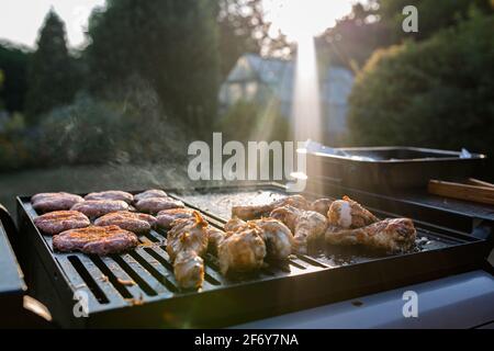 Nahaufnahme eines bbq-Grills mit Fleisch auf ihnen kochen, Sonneneinstrahlung im Hintergrund fängt den Rauch auf Stockfoto