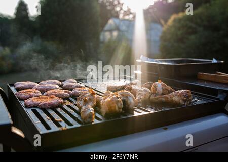 Nahaufnahme eines bbq-Grills mit Fleisch auf ihnen kochen, Sonneneinstrahlung im Hintergrund fängt den Rauch auf Stockfoto