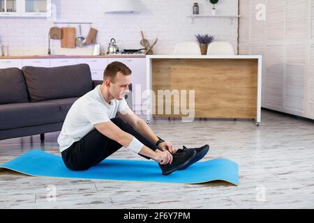 Ein junger Mann geht zu Hause zum Sport, bindet die Schnürsenkel vor dem Training an Turnschuhe. Gesunder Lebensstil Stockfoto