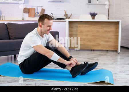 Ein junger Mann geht zu Hause zum Sport, bindet die Schnürsenkel vor dem Training an Turnschuhe. Gesunder Lebensstil Stockfoto