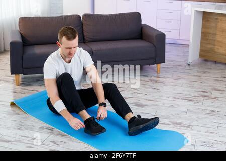 Ein junger Mann geht zu Hause zum Sport, bindet die Schnürsenkel vor dem Training an Turnschuhe. Gesunder Lebensstil Stockfoto