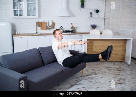 Ein junger Mann geht zu Hause zum Sport, er macht Liegestütze auf der Couch. Gesunder Lebensstil Stockfoto