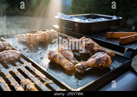 Nahaufnahme eines bbq-Grills mit Fleisch auf ihnen kochen, Sonneneinstrahlung im Hintergrund fängt den Rauch auf Stockfoto